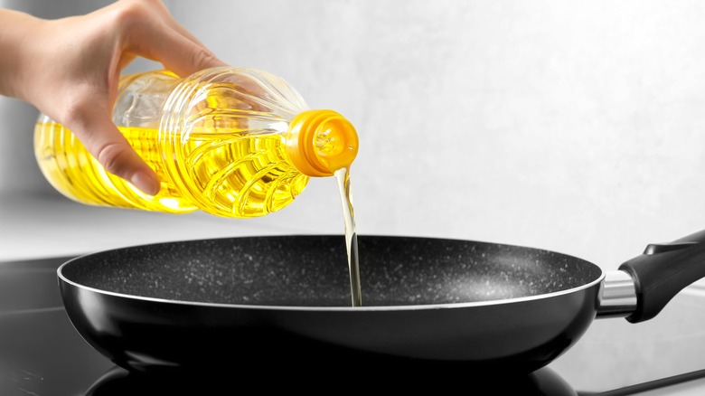 Woman pouring cooking oil into a frying pan