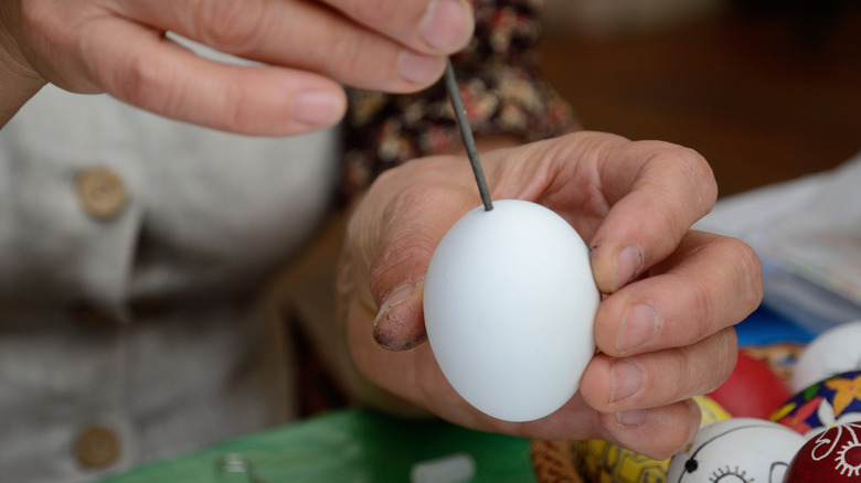 Person piercing egg with nail