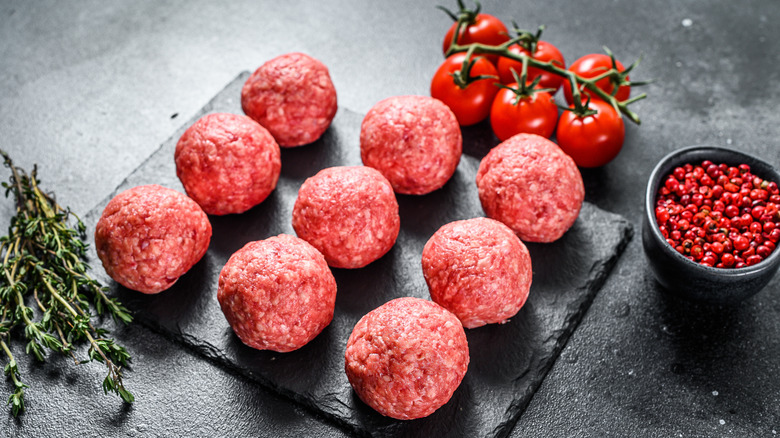 Raw meatballs on black slate with thyme and tomatoes