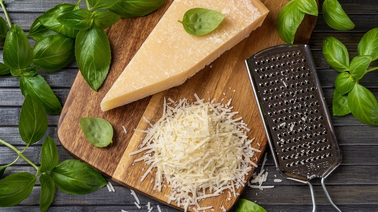 Grated hard cheese on board with grater and basil leaves