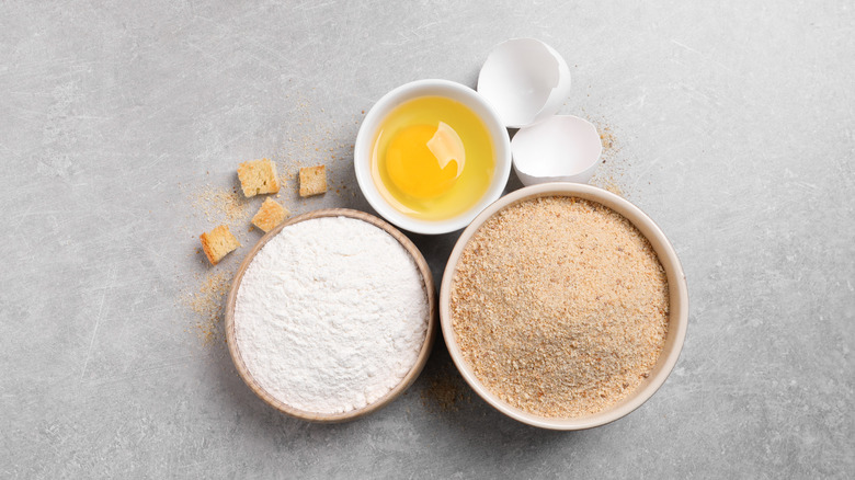 Breadcrumbs, egg, and flour in dishes gray background