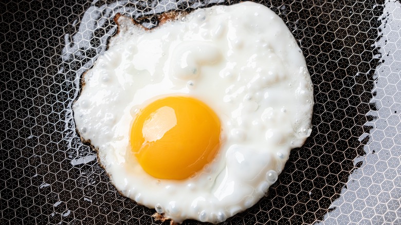 close-up of an egg frying in a black nonstick pan.