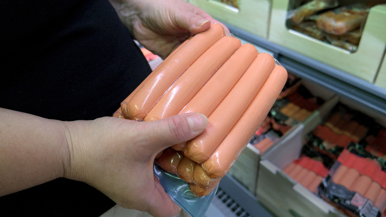 Person holding package of hot dogs in supermarket