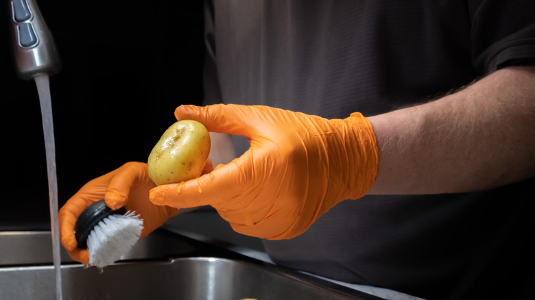 man cleaning potato with brush