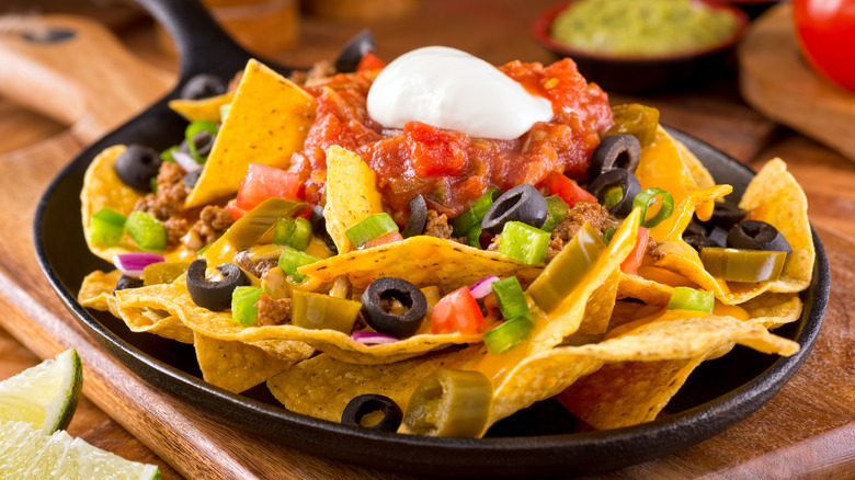 skillet of tortilla nachos topped with salsa and sour cream