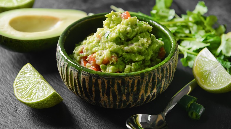 fresh guacamole in bowl with lime wedges