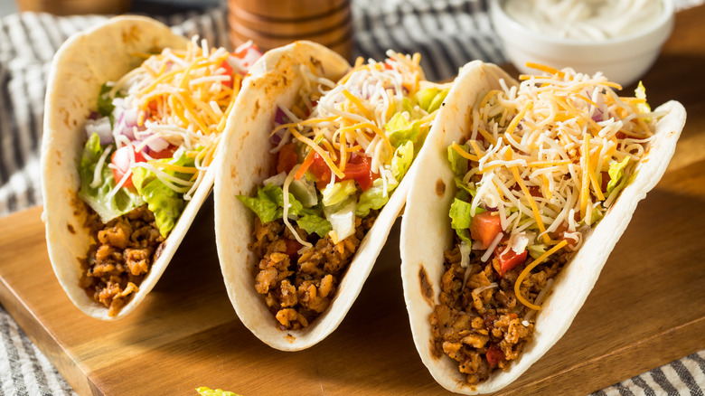 three tacos topped with lettuce tomatoes and shredded cheese