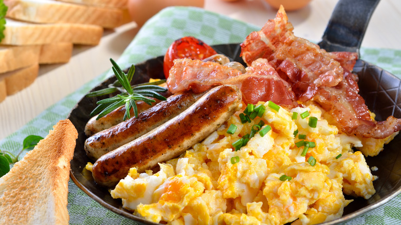 a plate with sausage, bacon, eggs, and a piece of toast