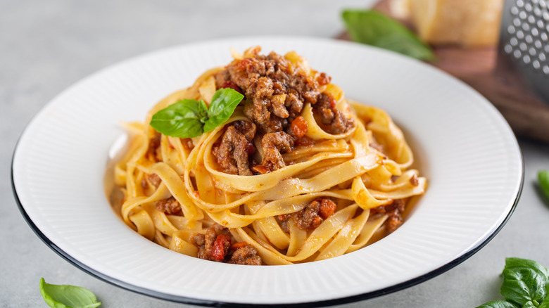 a bowl of pasta, sauce, meat crumbles, and oregano leaf