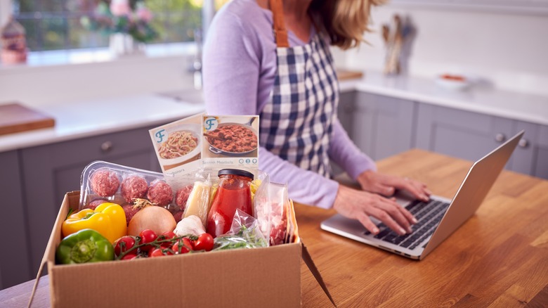 woman on laptop next to box of veggies and sauces