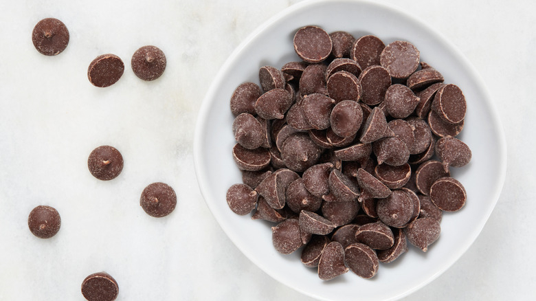 Bowl of chocolate chips, with chocolate chips to the side of it