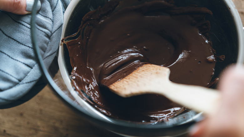 Bowl of melted chocolate being stirred with wooden spatula