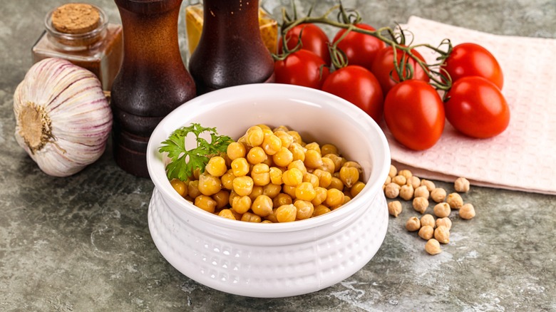 Bowl of cooked chickpeas surrounded by garlic, tomatoes, and spices.