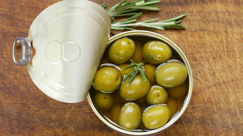 Open can of green olives with a sprig of rosemary