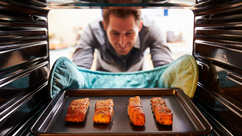 man taking salmon from oven