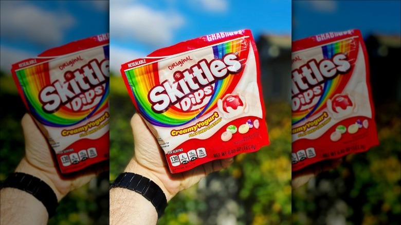 a hand holding a bag of skittles dips