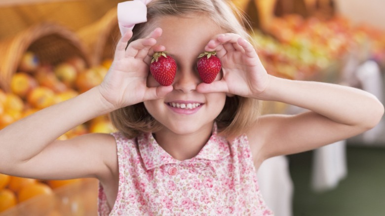 Girl holding strawberries over her eyes