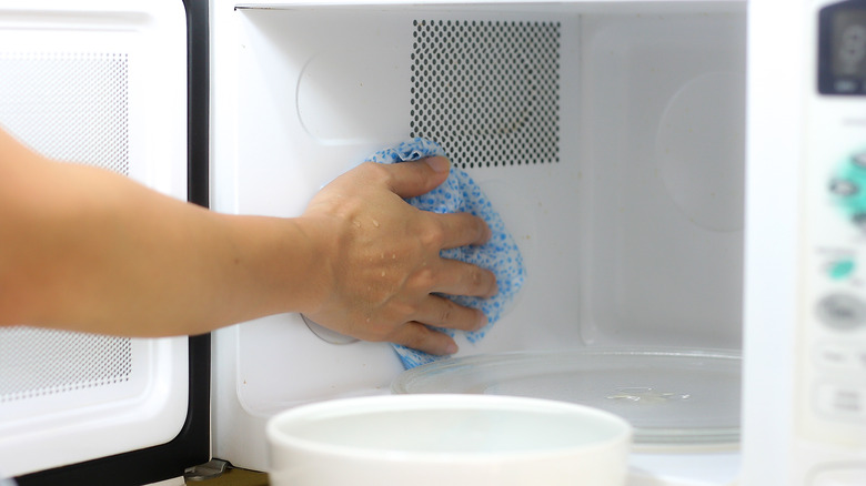 person cleaning microwave