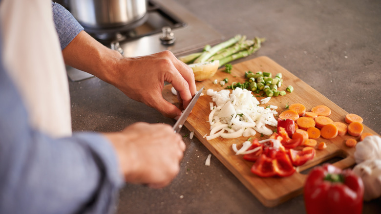 Hands chopping vegetables on board