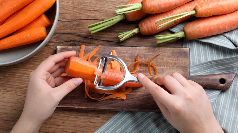 Hands peeling carrots on board