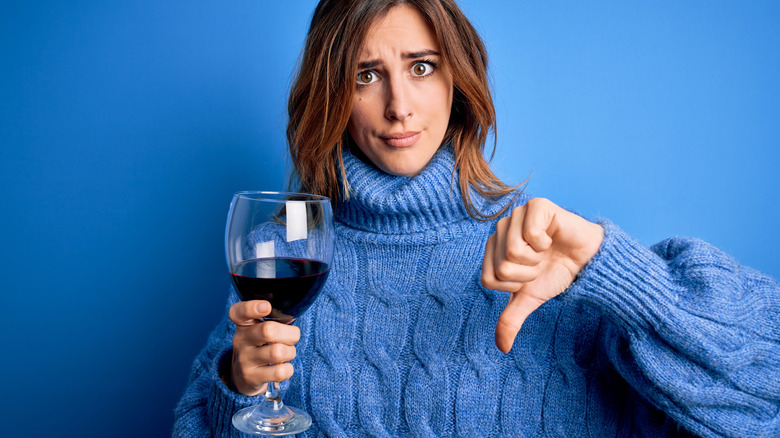 woman in blue holding wine doing thumbs down