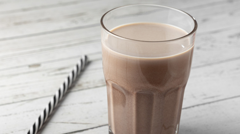 A glass of chocolate milk sits on a table beside a straw