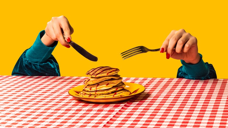 Hands slicing plate of pancakes