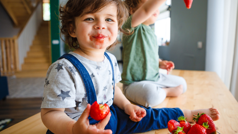 toddler in overalls eating strawberries