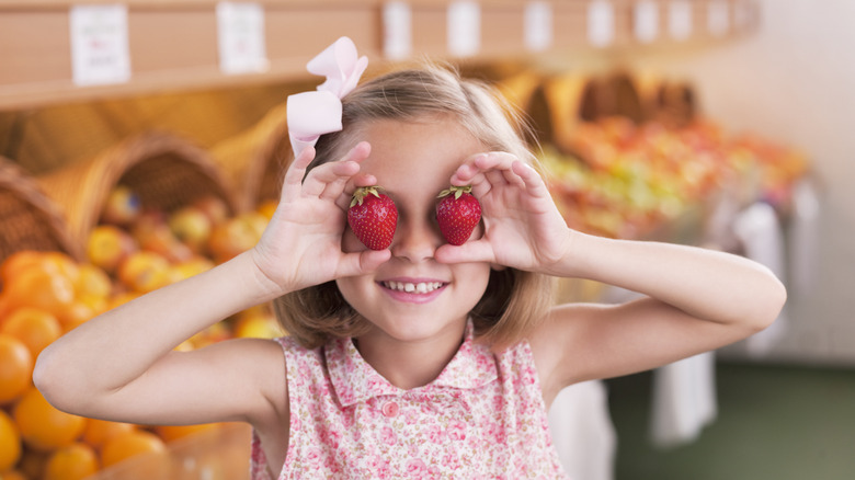 child holding strawberries to her eyes 