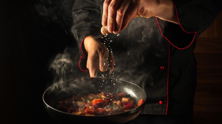 Chef adding salt to pan