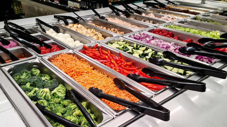 brocoli, carrots, red pepper, cucumber, black tongs, metal counter, salad bar