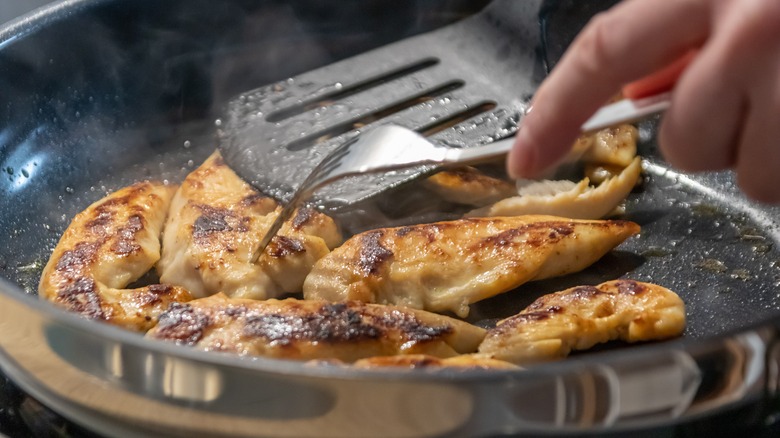 person cooking chicken in pan