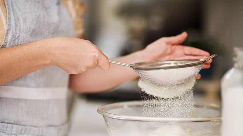 Person sifting flour into bowl