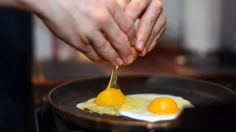 Person cracking eggs into frying pan
