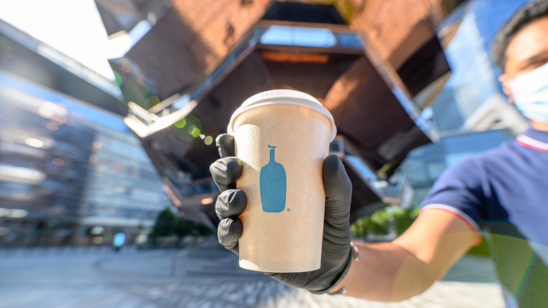 hand holding out Blue Bottle cup