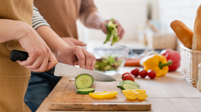 People cutting vegetables on board 