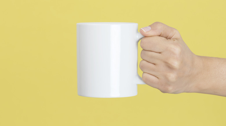 hand holding mug with yellow background