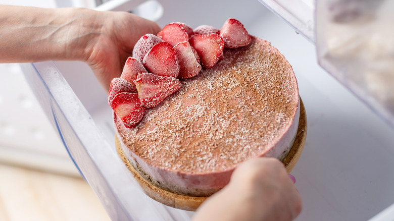 hands holding frozen cake with strawberries