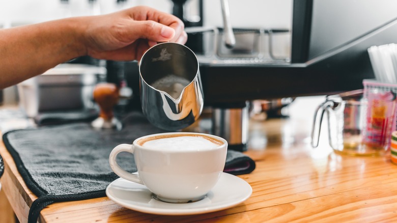 man pouring milk beside his home espresso machine