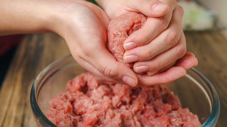 Two hands shaping raw meatballs