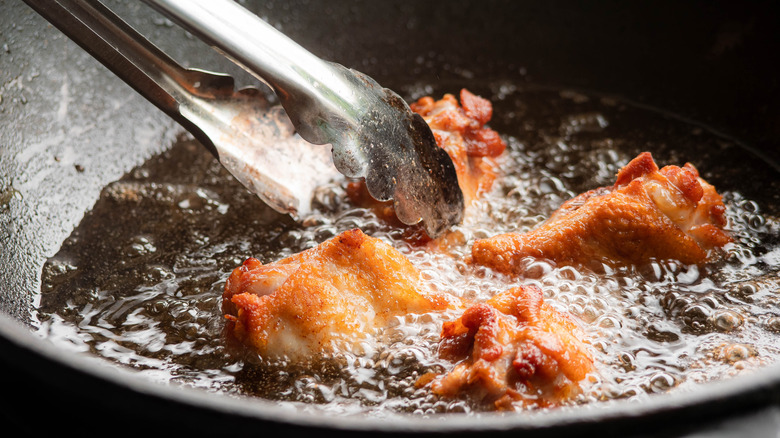 Tongs touching frying chicken