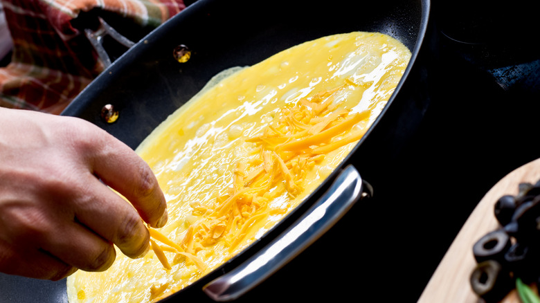 person adding cheese to omelet