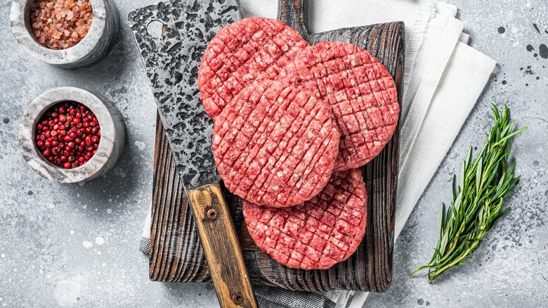 raw burger patties on wooden board