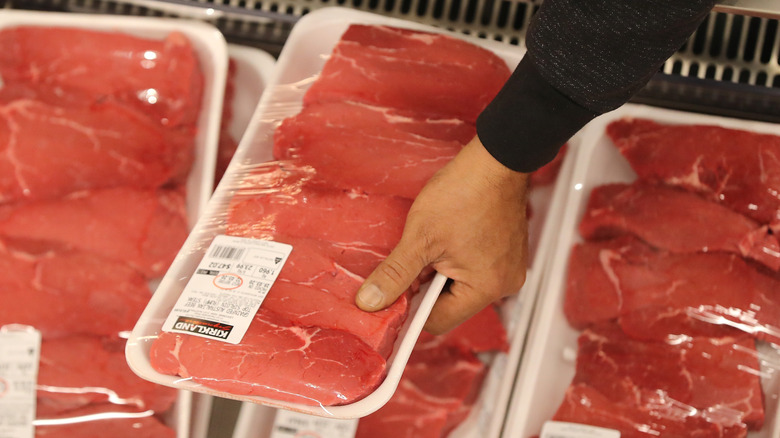 Person picking up package of Kirkland Signature top sirloin steaks