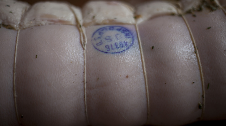 Porchetta tied with string, with blue stamp on its outer rind, indicating that it's been inspected