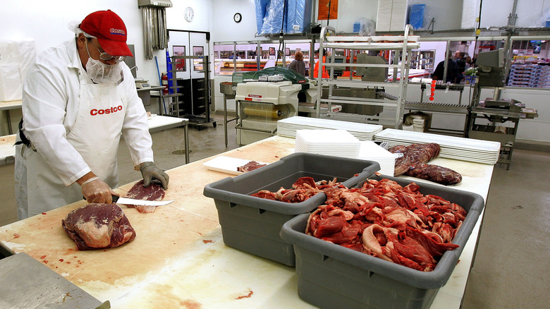 Costco butcher slices meat in-store, with boxes of fresh meat on table next to him