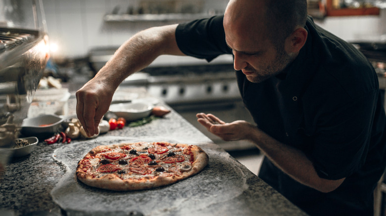 Chef putting finishing touches on freshly-cooked pizza