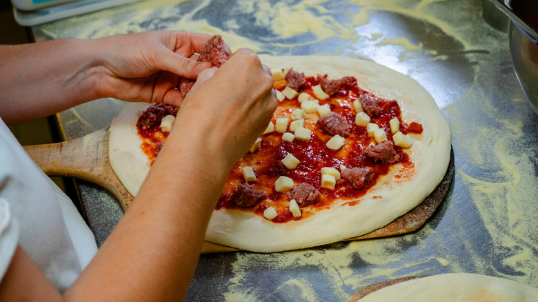 Chef making pizza in restaurant, placing toppings onto the base