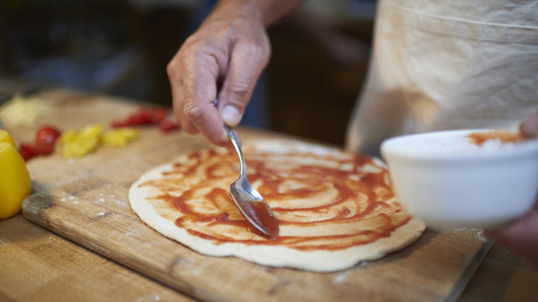 Chef swirling tomato sauce onto pizza base