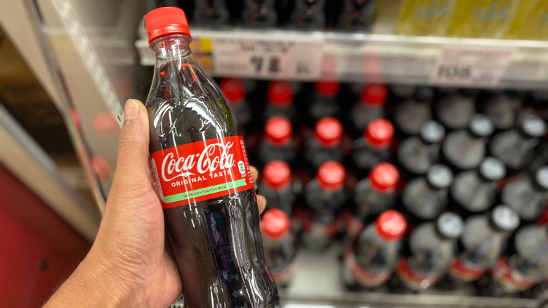 Person holding Japanese Coca-Cola bottle in convenience store, with multiple bottles blurred out behind it